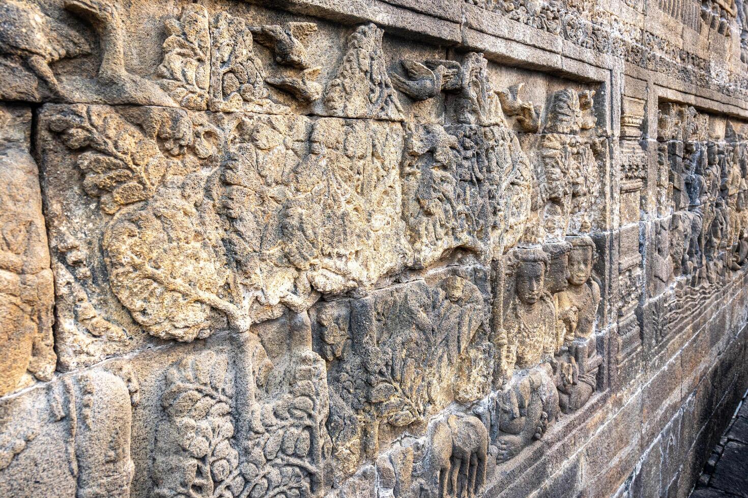 Stone wall carvings show ancient scenes with trees, people, birds, and animals in fine detail. photo