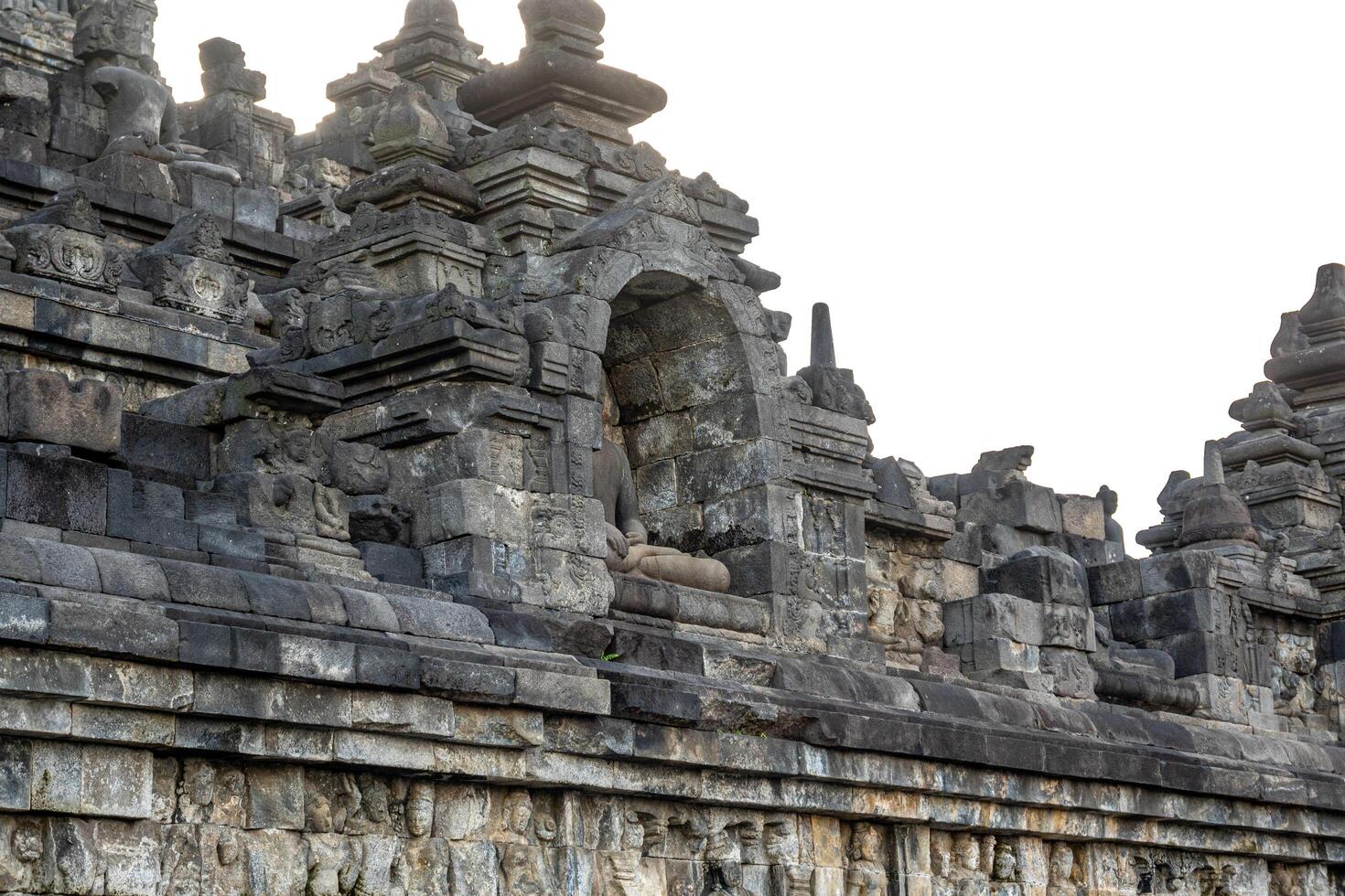 A headless Buddha statue sits in a stone niche on Borobudur temples ancient upper terrace. photo