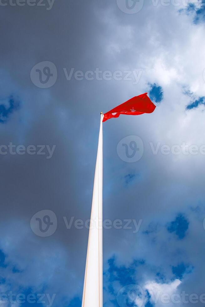 Red Flag on Tall Pole Against Blue Sky with Clouds A Stunning Vertical Photograph photo