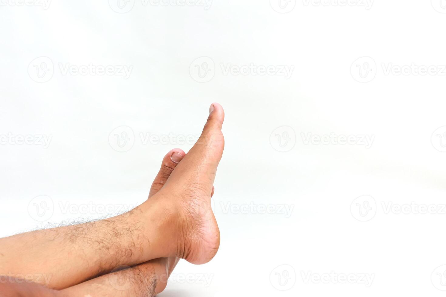 Close-up shot of crossed legs with foot pointing upward against a white backdrop, creating negative space photo