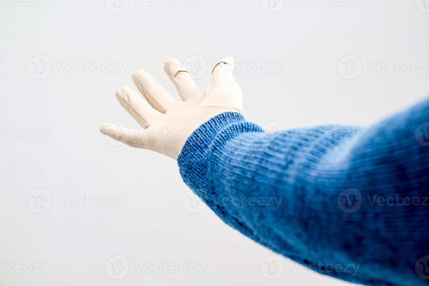 Hand in latex glove reaching out from a blue knitted sweater sleeve with plaster on finger photo