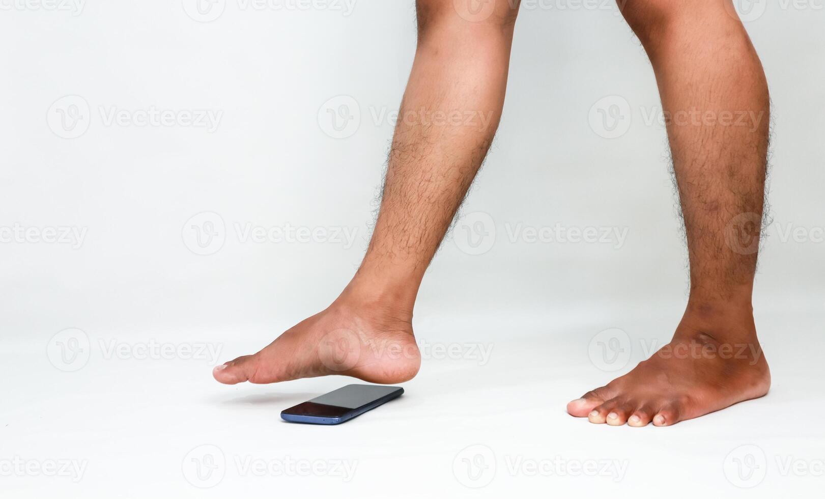 Foot about to step on a smartphone on a white background, a cautionary or destructive scenario for technology photo