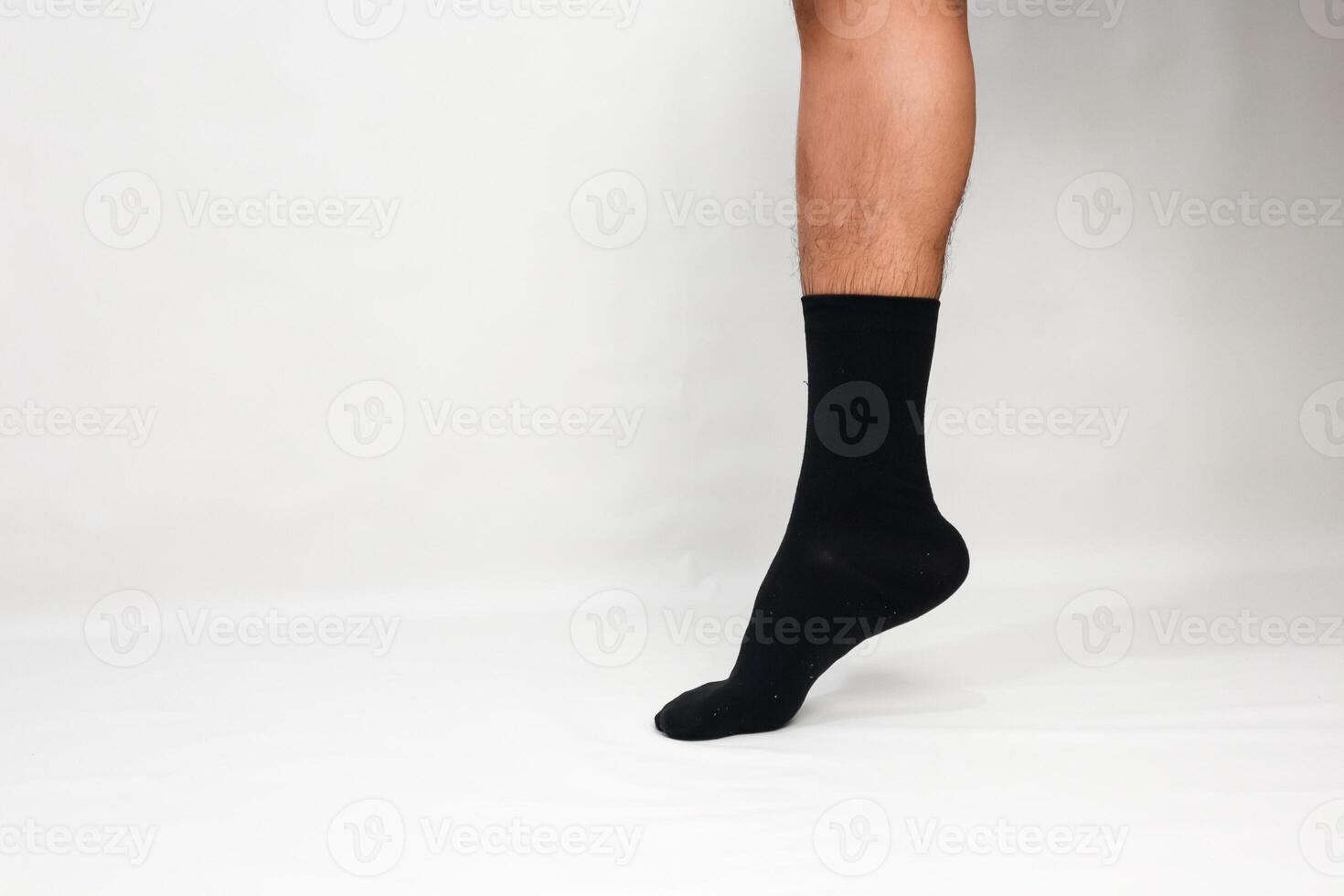 A man's leg and foot clad in a sleek black sock against a minimalist white backdrop photo