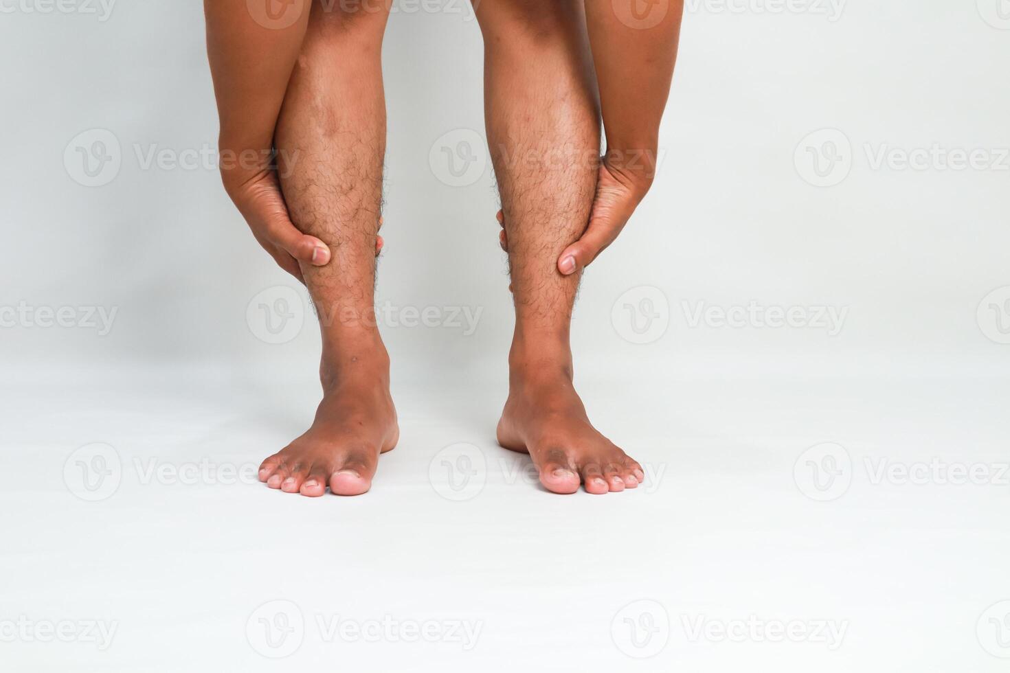 Man holds his legs, expressing leg pain or muscle cramp issues on a plain background photo