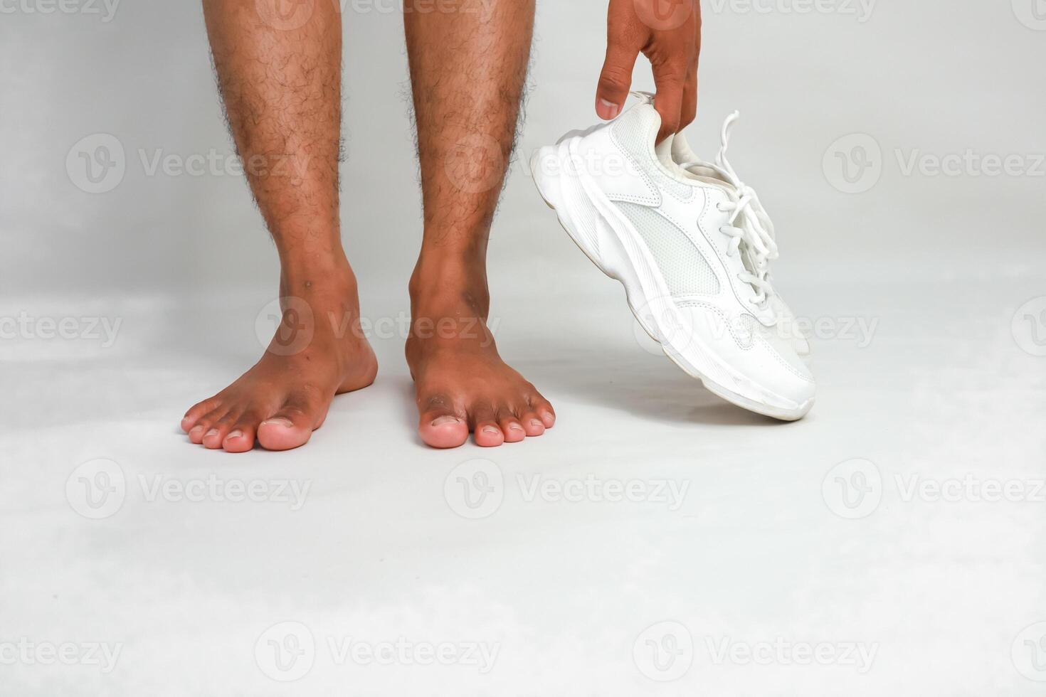 Barefoot man holding a white sneaker, presenting a contrast between comfort and formal wear photo
