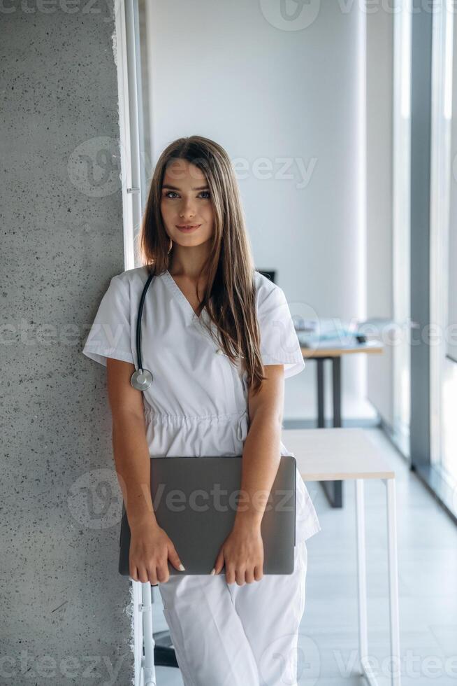 Laptop is in hands. Professional female doctor in the clinic indoors photo