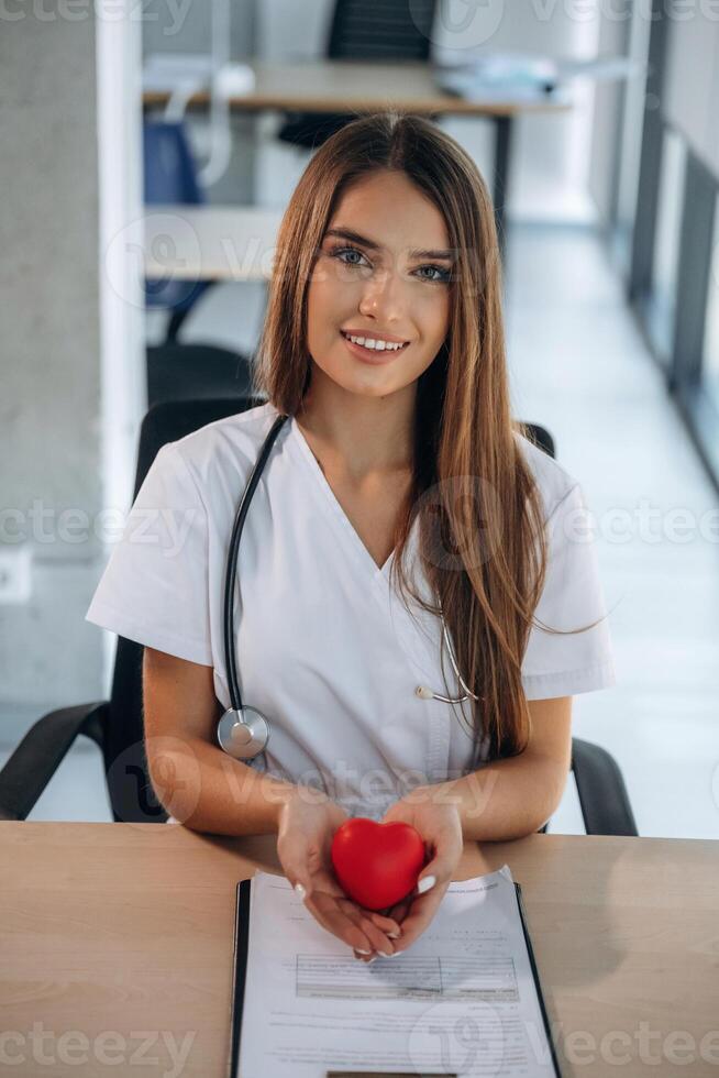 Heart care conception, holding little toy. Professional female doctor in the clinic indoors photo