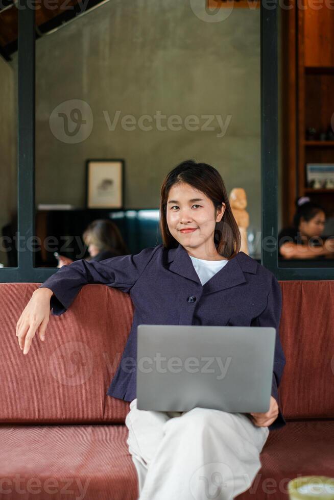 Woman sitting on a sofa with a laptop in a modern cafe, exuding confidence and relaxation. photo