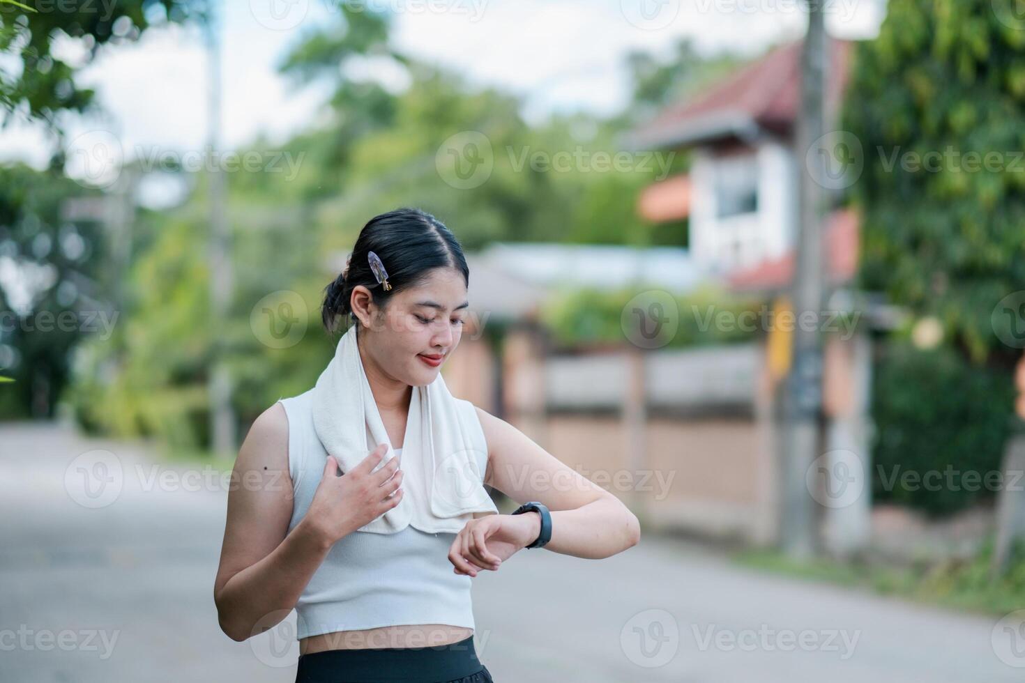 Young woman in athletic wear checking her smartwatch while exercising outdoors in a suburban area with greenery. photo