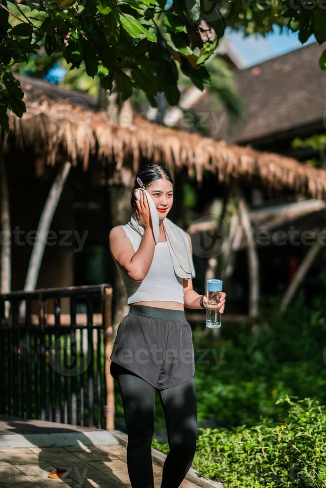 Woman in athletic wear with water bottle, enjoying a sunny day in a green park setting. photo