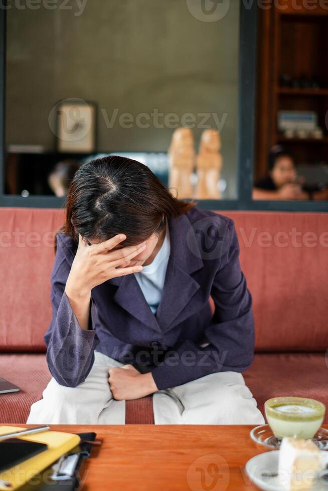 Woman in a cafe looking stressed, sitting with hand on forehead, reflecting in a cozy setting. photo