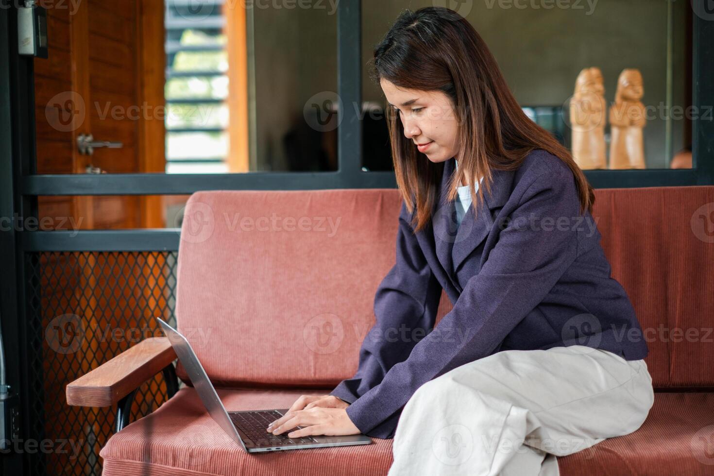 A focused young woman using a laptop while sitting on a comfortable sofa in a stylish home office environment. photo