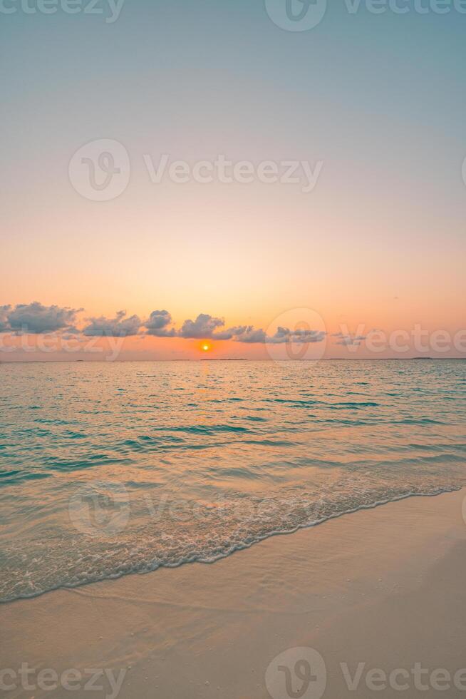 Sunset beach closeup vertical view showing calm sea, soft sand, and warm colorful sky, tranquil tropical nature scene inspiring peaceful vacation, travel, and serene beach moments photo