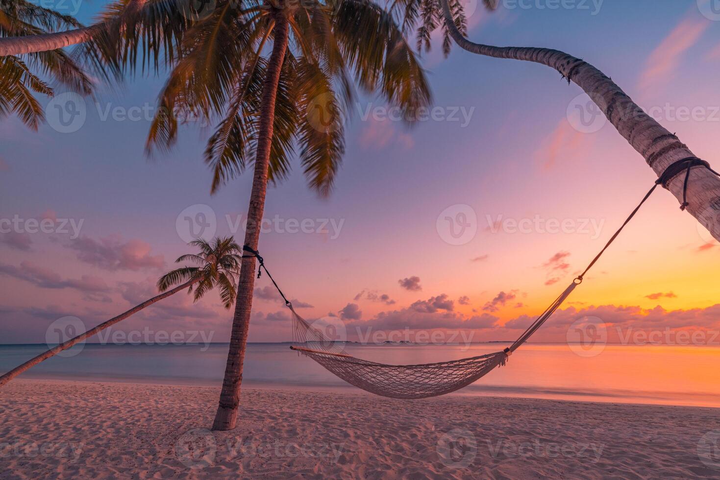 Gorgeous sunset beach with hammock strung between palm trees, relaxing tropical island escape with peaceful tranquil nature, serene summer vacation landscape for carefree travel and leisure photo
