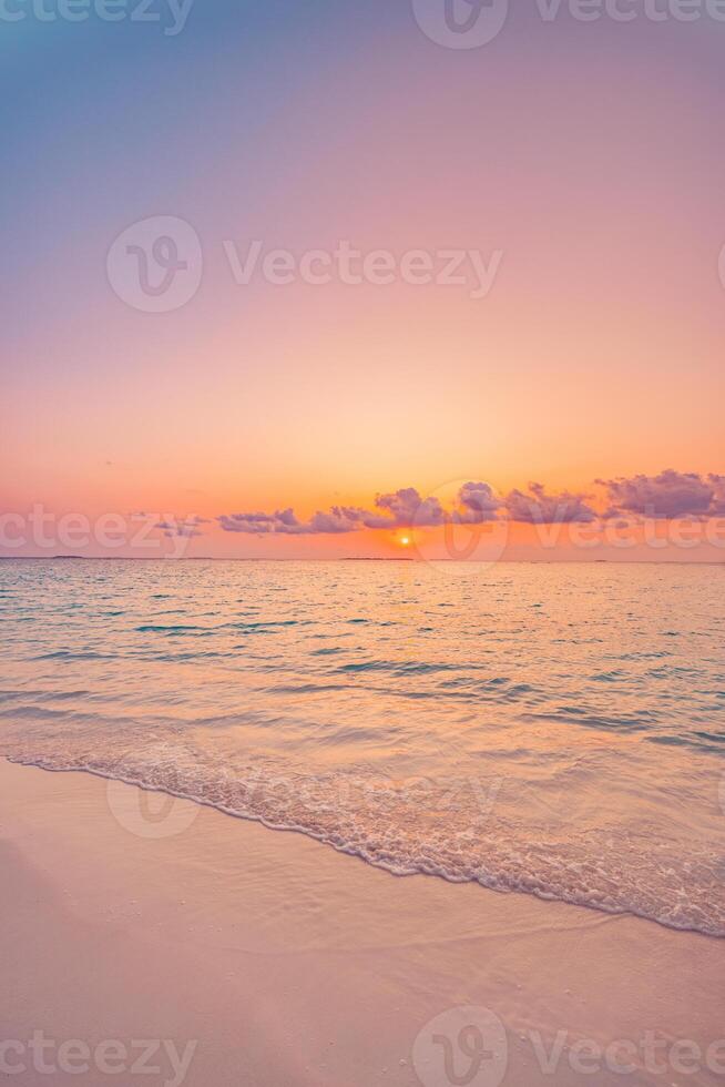 Vertical closeup of sunset beach with golden sand, calm sea waves, vibrant colorful sky, serene tropical landscape, peaceful nature scene perfect for travel, vacation, and relaxation vibes photo