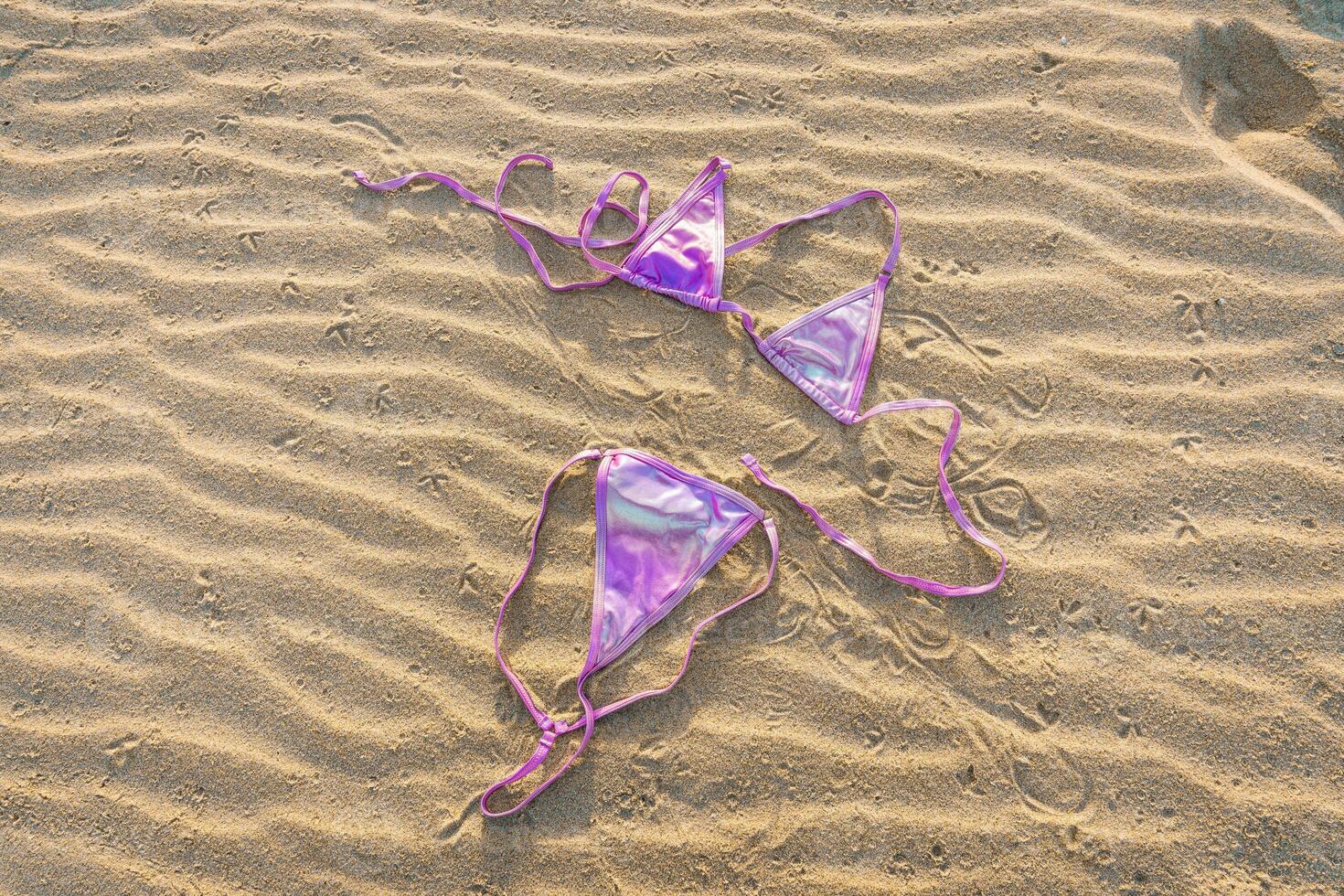 Pink Iridescent Bikini Lying On Sand Textured Background photo
