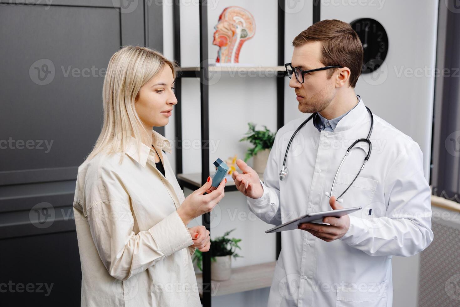 Male doctor holding in hand an aerosol inhaler on a demonstration to a female patient at office. photo