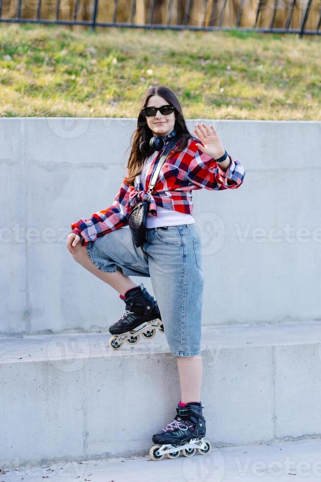 Stylish teenager waving while posing with inline skates in an urban setting photo