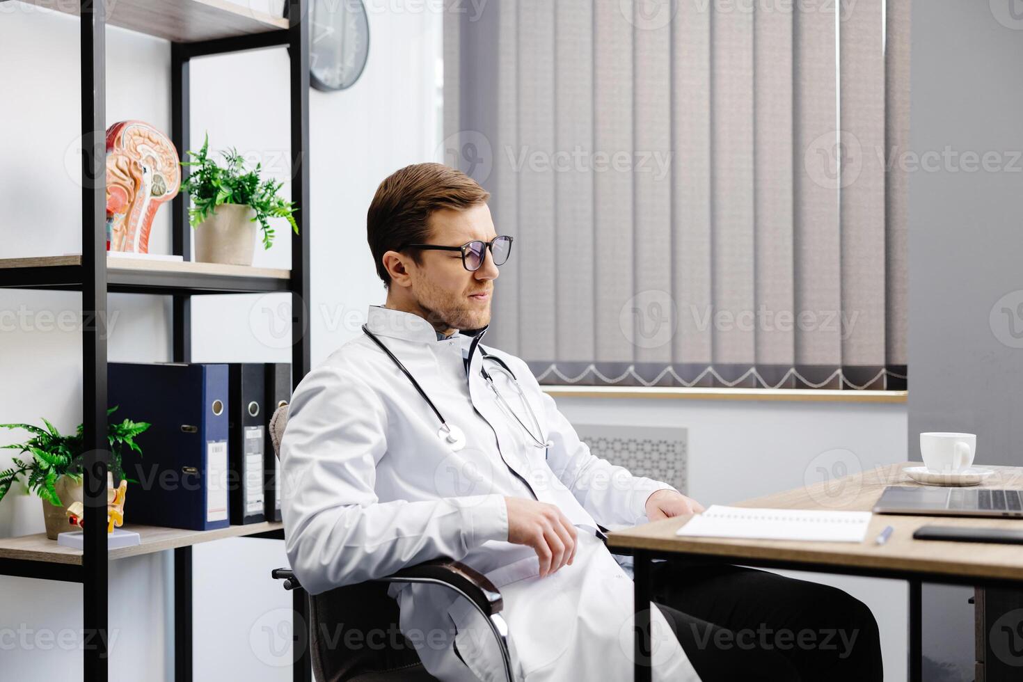 Doctor sits at his workplace and feels tired from work. A doctor takes a break from his work day because of pain photo