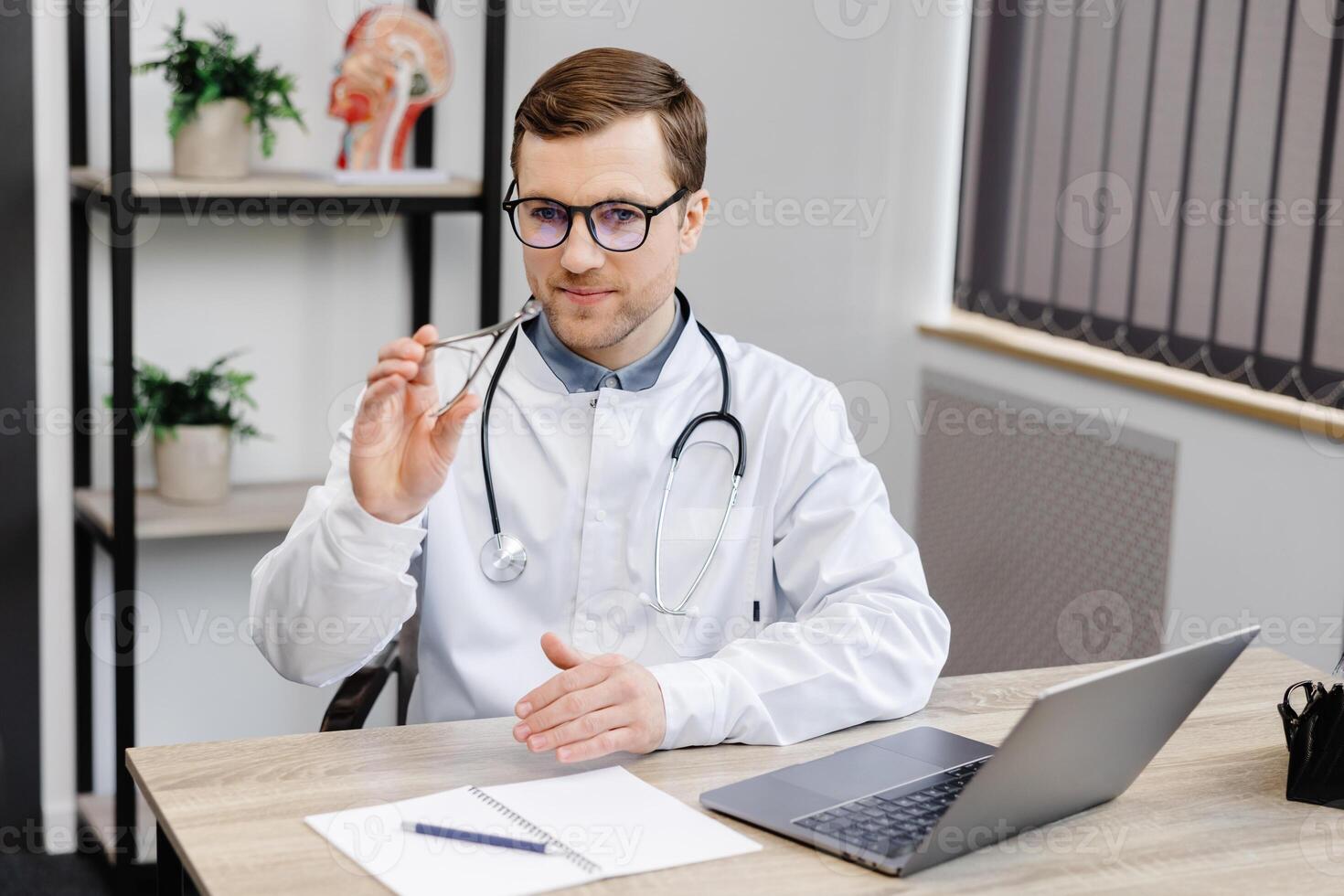 Young otolaryngologist doctor sitting at his workplace in the office and holding a nose mirror. photo