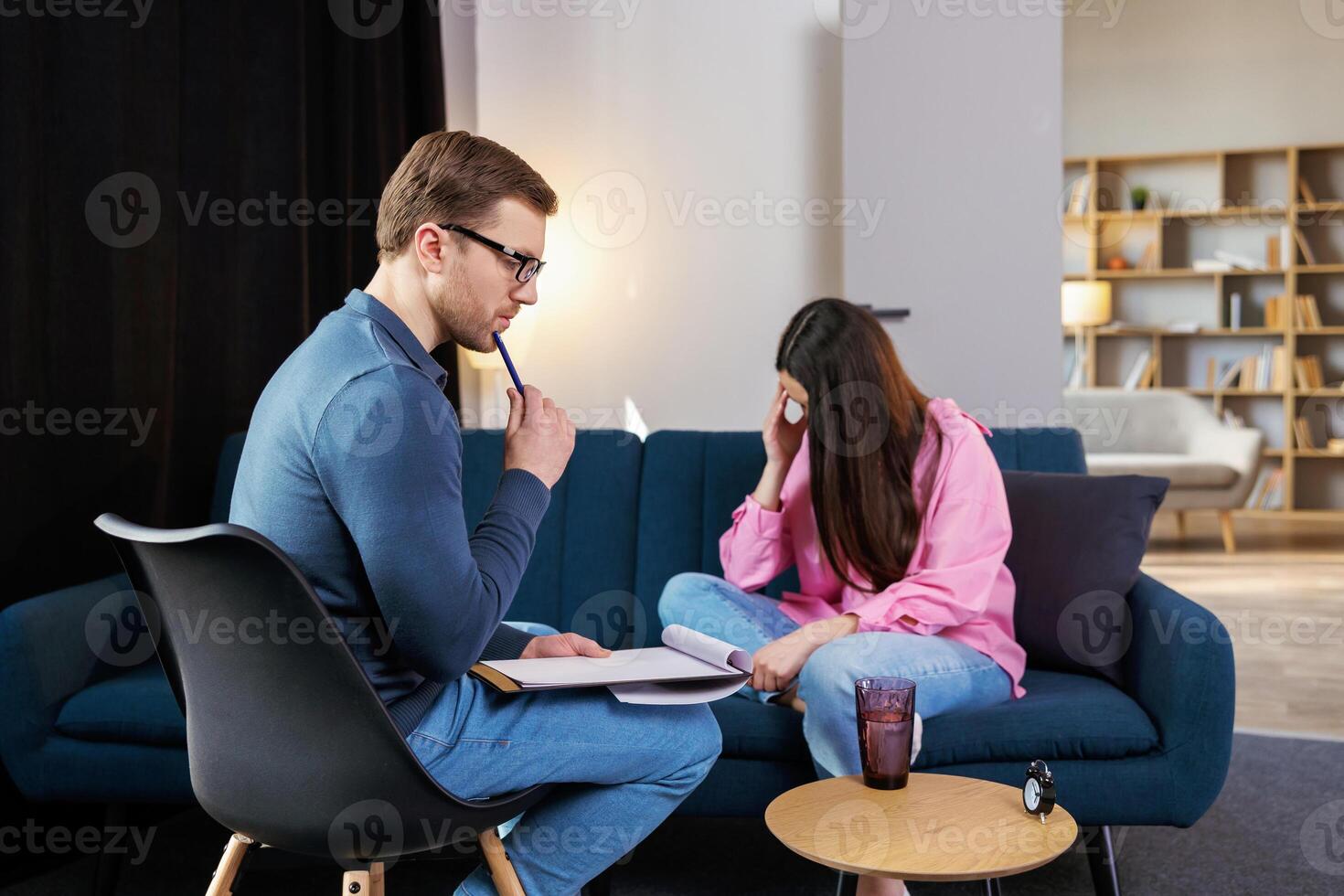 Woman having session with psychologist, sitting on couch at clinic. The woman is very upset, the psychotherapist is trying to help her with the problem photo