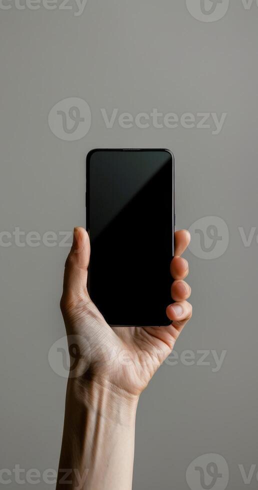 A person holding up a black smartphone with a blank screen photo