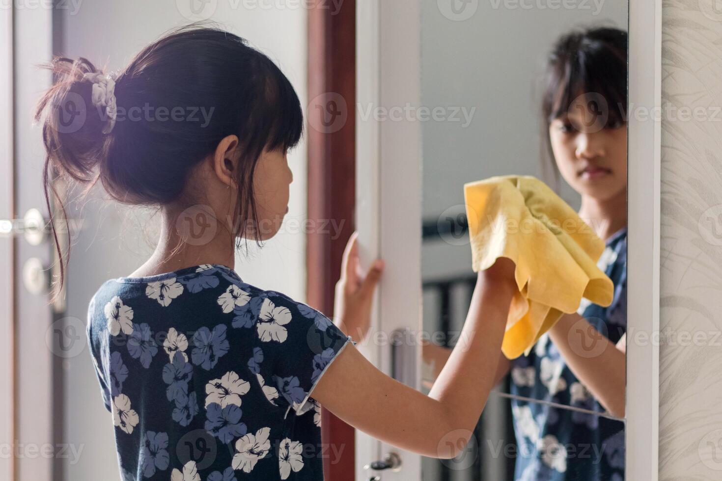 Household chores for children. A young Asian girl wiping the mirror in the wardrobe with a chamois cloth photo