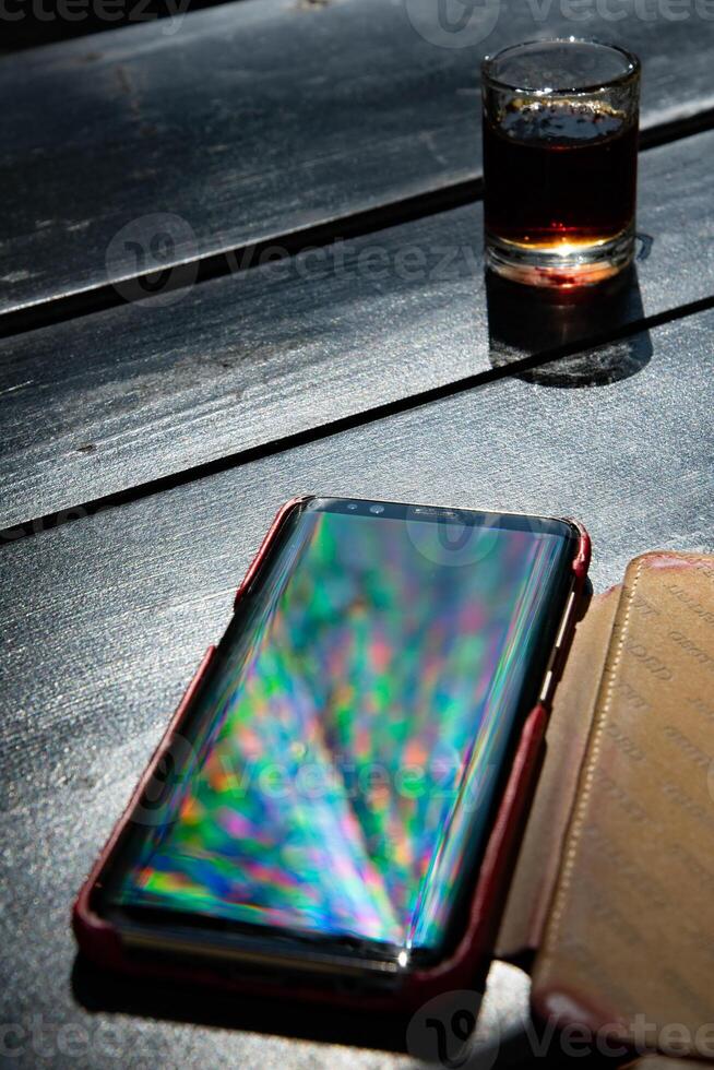 Spectrum blur reflection in glossy surface of smartphone on black table with alcohol drink shot photo