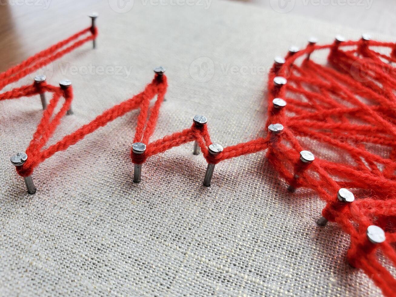 Creative string art project featuring vibrant red yarn and nails on fabric, depicting geometric patterns in numerous shapes and lines, showcasing artistic expression and craftsmanship skills photo