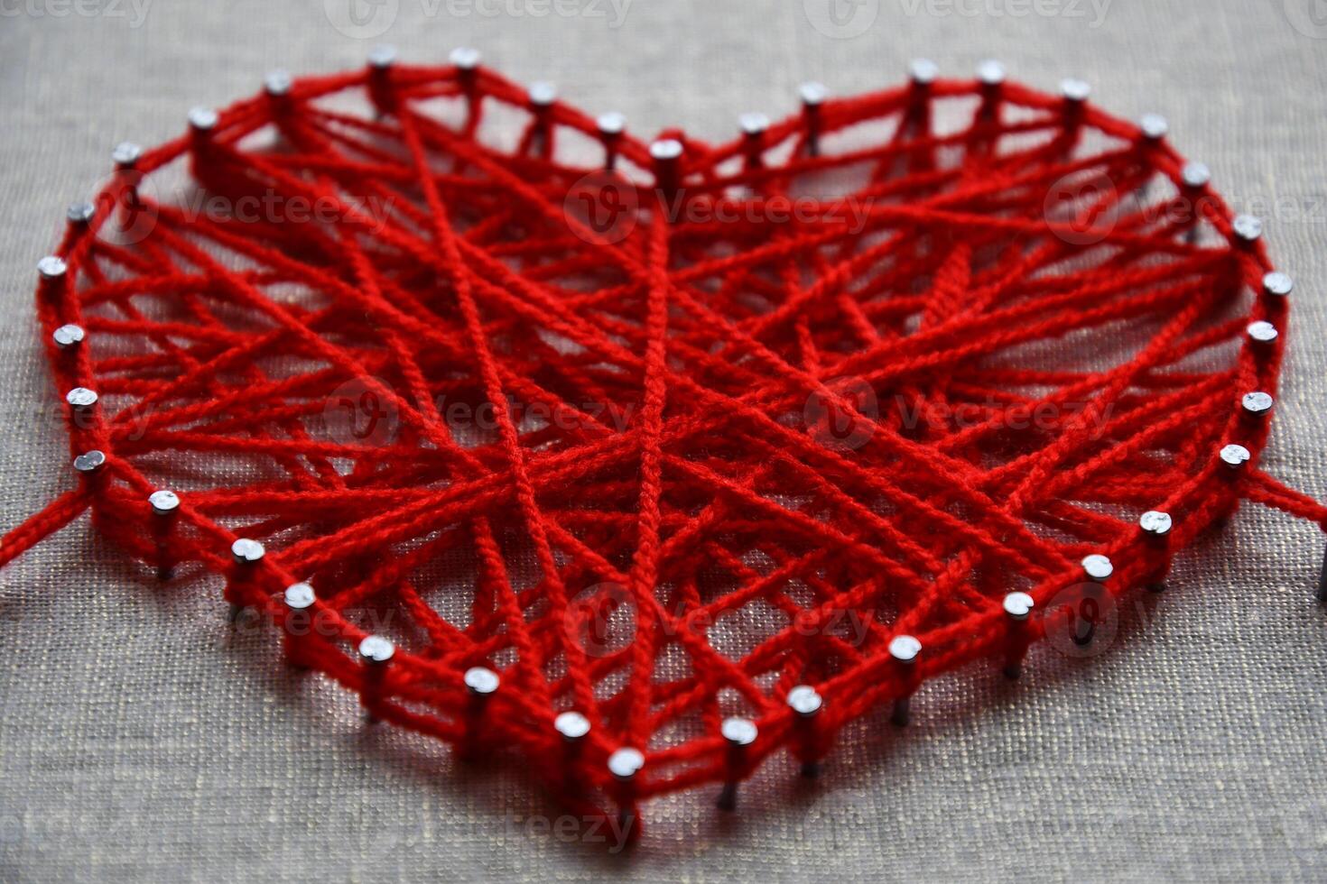 Red heart string art made with tangled yarn on metal nails on canvas background photo