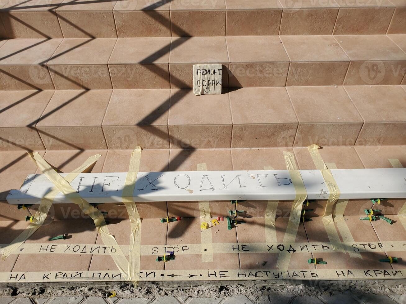 Tiled stairs renovation and warning red striped tape. Construction background with zig zag shadow pattern on staircase. Cement steps with tapes and text - do not step, renovation, sorry photo