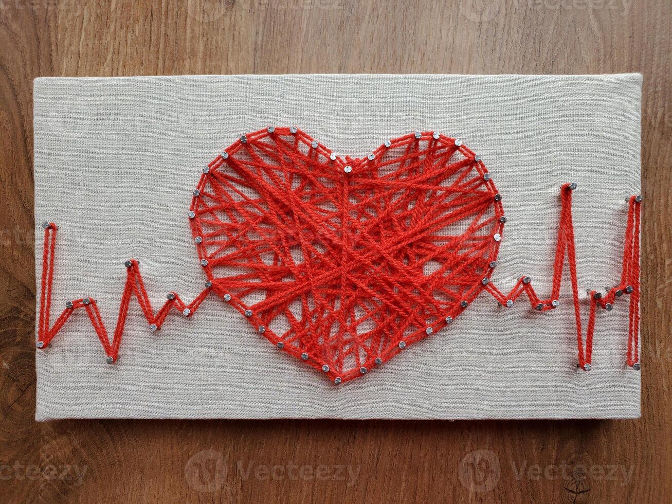 Heart crafted with vibrant red string art displaying heartbeat rhythm on textured canvas surface showcasing intricate design and creative expression using simple materials and colors photo