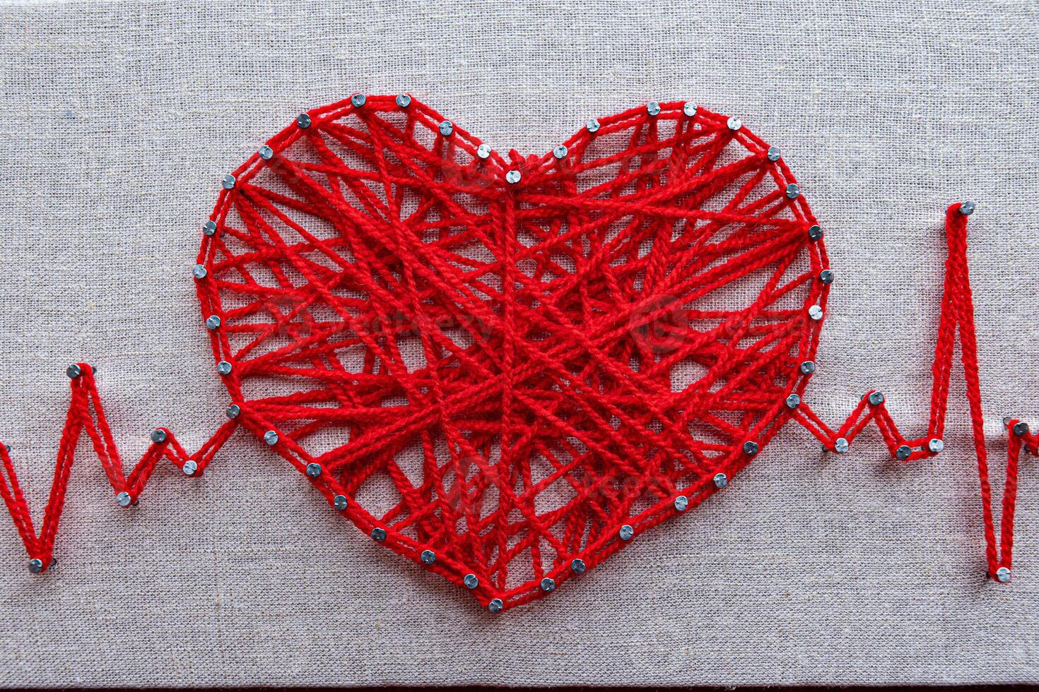 Red heart and heartbeat lines string art made with tangled red yarn on metal nails at canvas texture photo