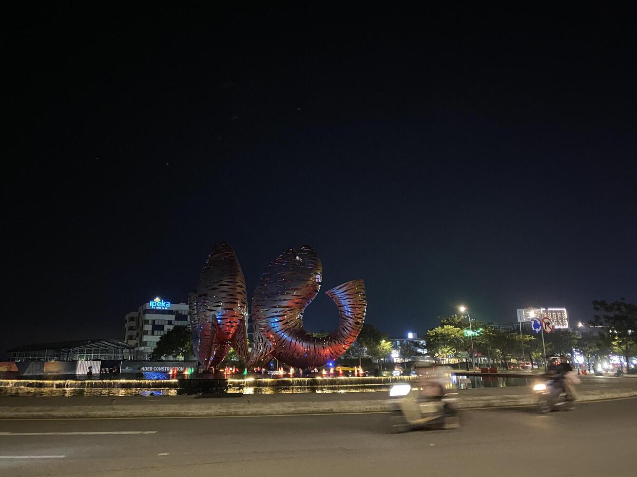 Illuminated abstract sculpture graces a roundabout at night with blurred motion and city lights. photo