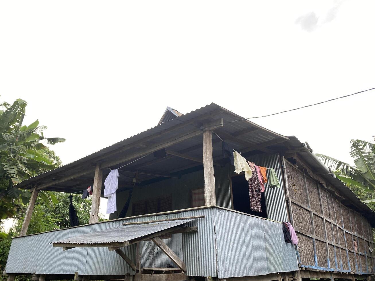 Rustic dwelling stands amidst lush greenery with laundry drying in the tropical air. photo