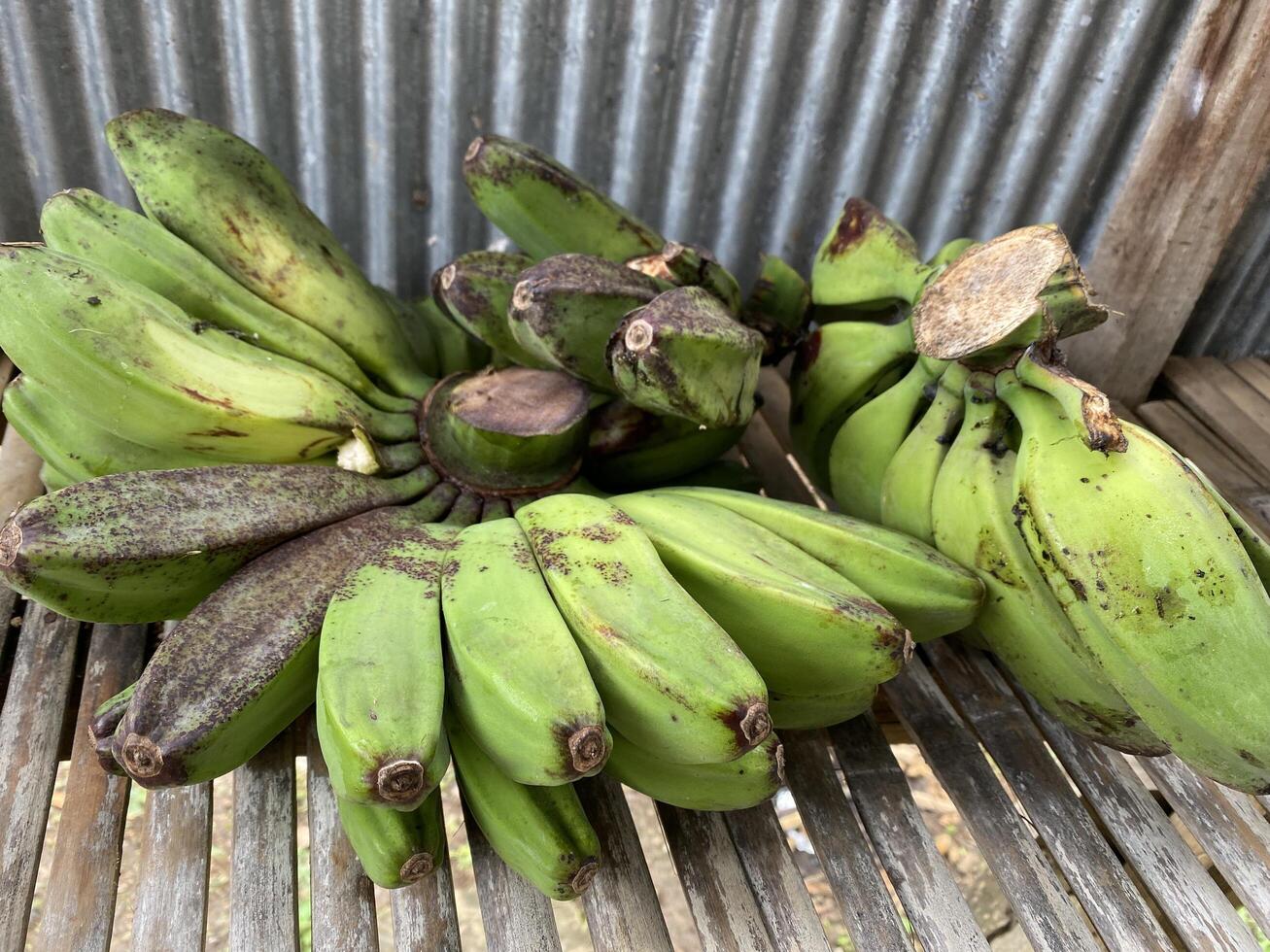 Unripe bananas cluster together on a weathered wooden waiting to ripen naturally. photo