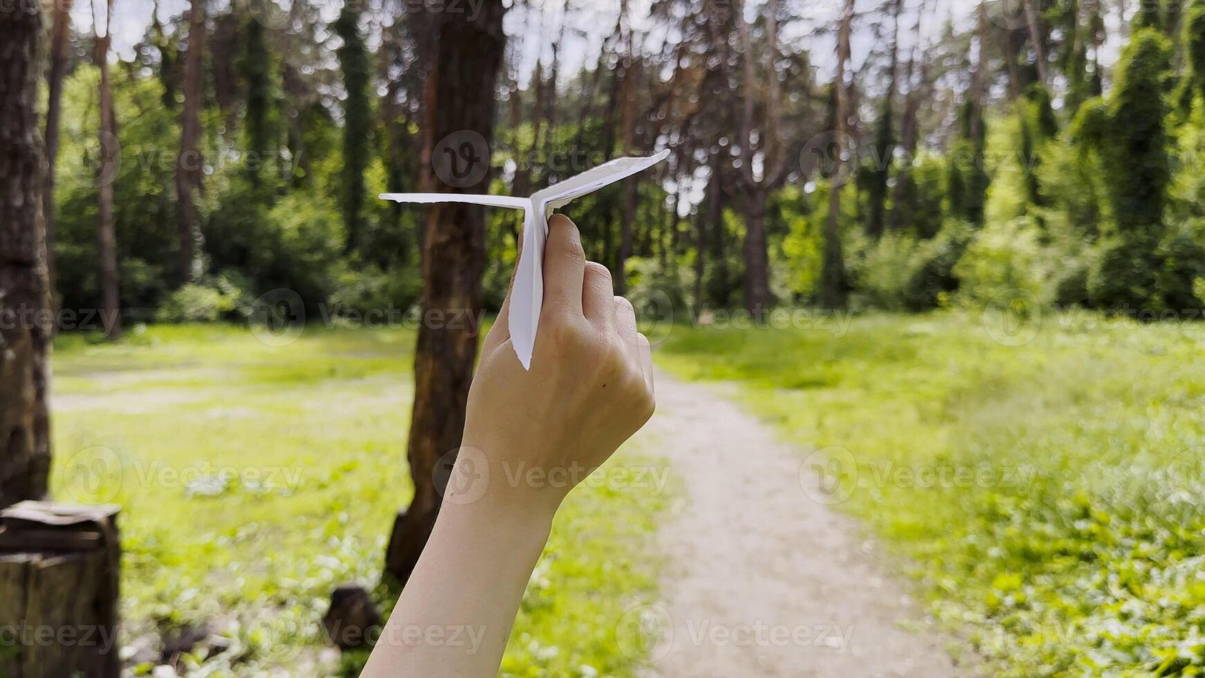 Female hand playin with paper airplane at summer forest. Girl walking with toy plane at woodland on sunny day. Young woman having fun at nature. Concept of leisure outdoor. Close up photo