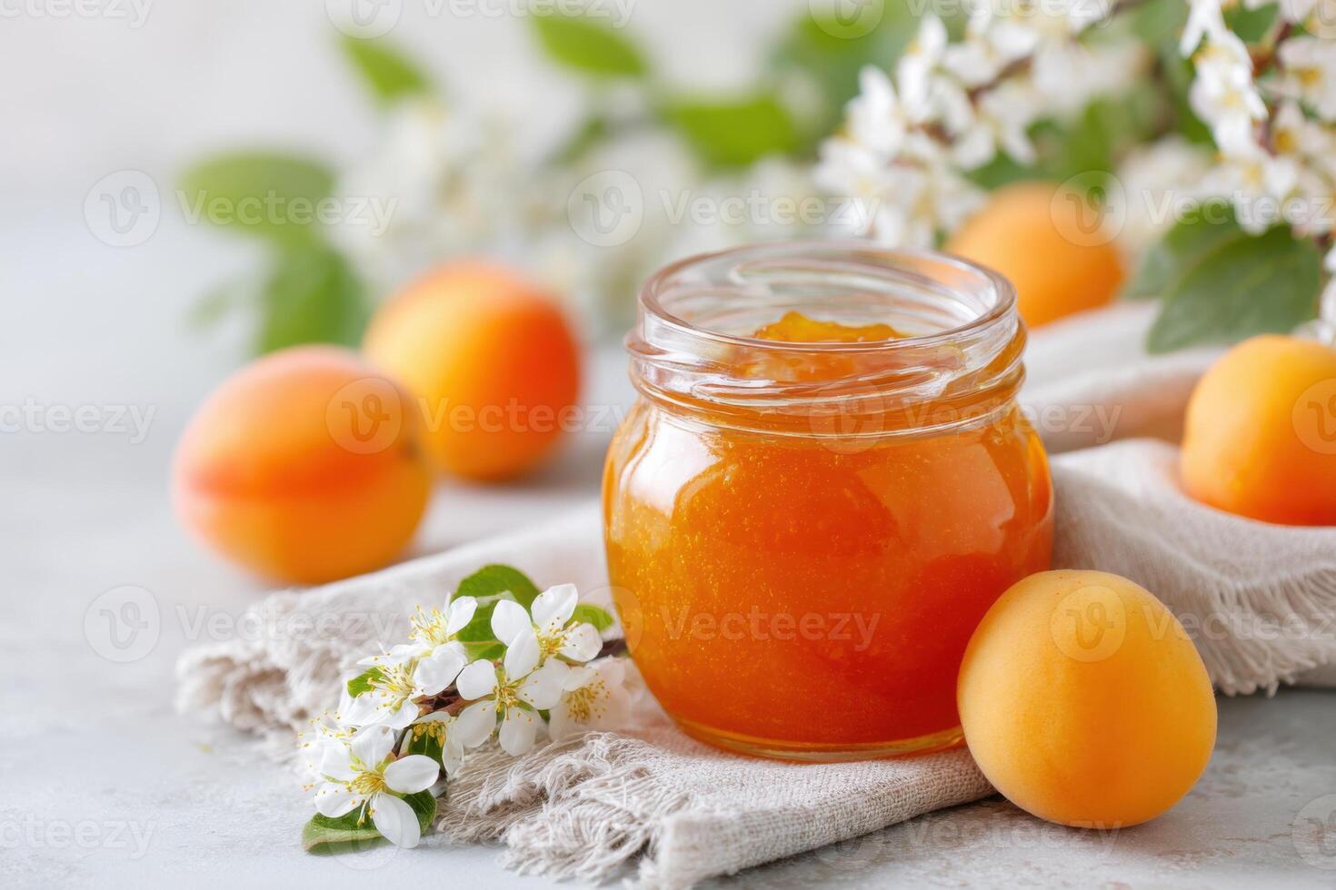 Jar of homemade apricot jam surrounded by fresh apricots and delicate white flowers on a textured linen cloth, showcasing a vibrant and inviting culinary scene photo