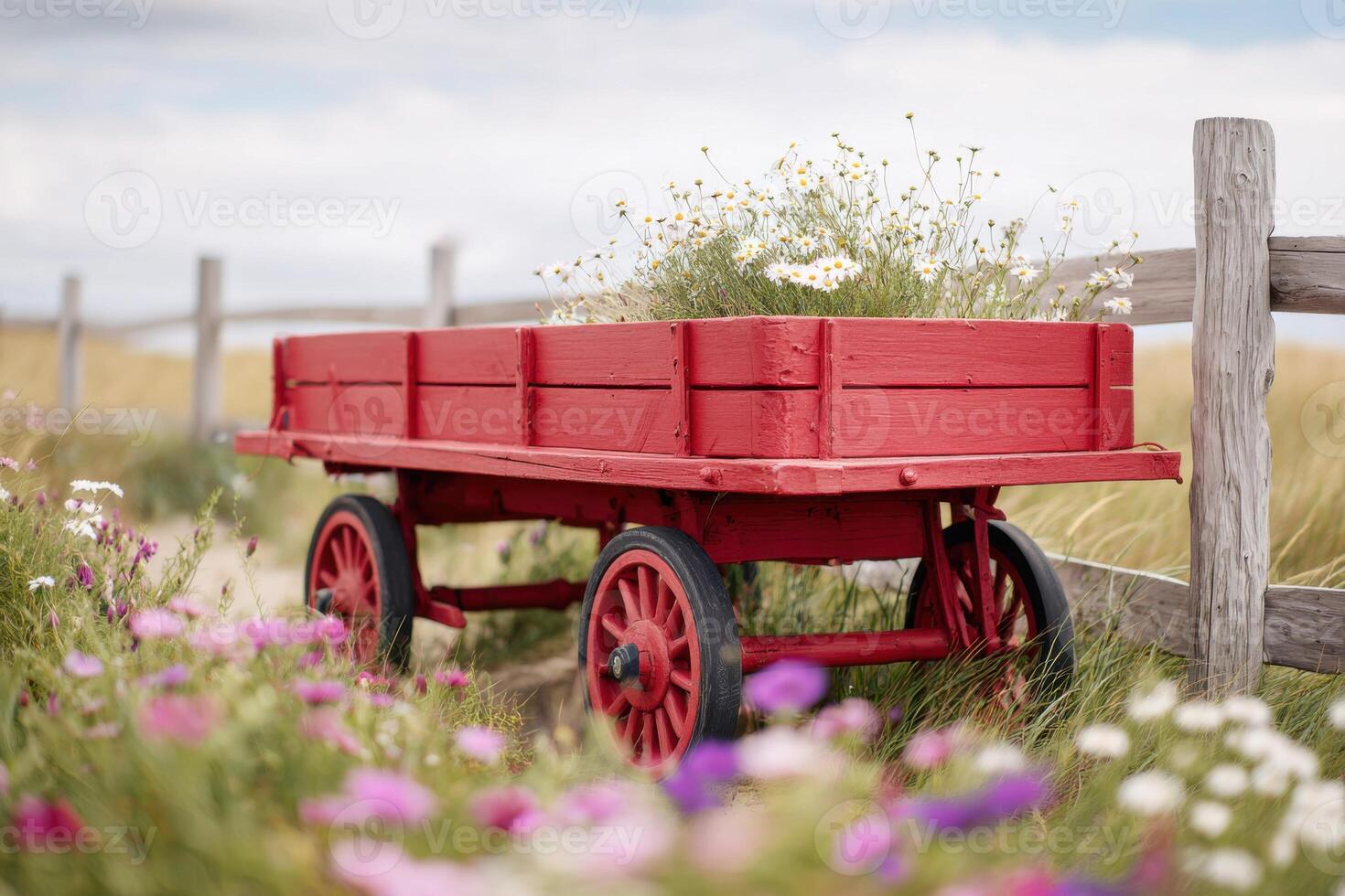 Red wooden wagon filled with wildflowers stands beside a rustic wooden fence in a vibrant field, showcasing a picturesque rural landscape with natural beauty photo