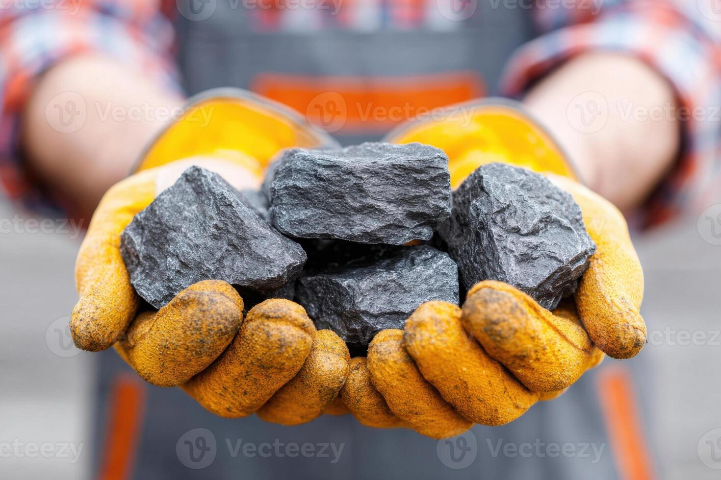 Individual wearing yellow gloves holds several pieces of black coal in hands, showcasing the raw material's texture and weight, emphasizing the importance of coal in energy production photo