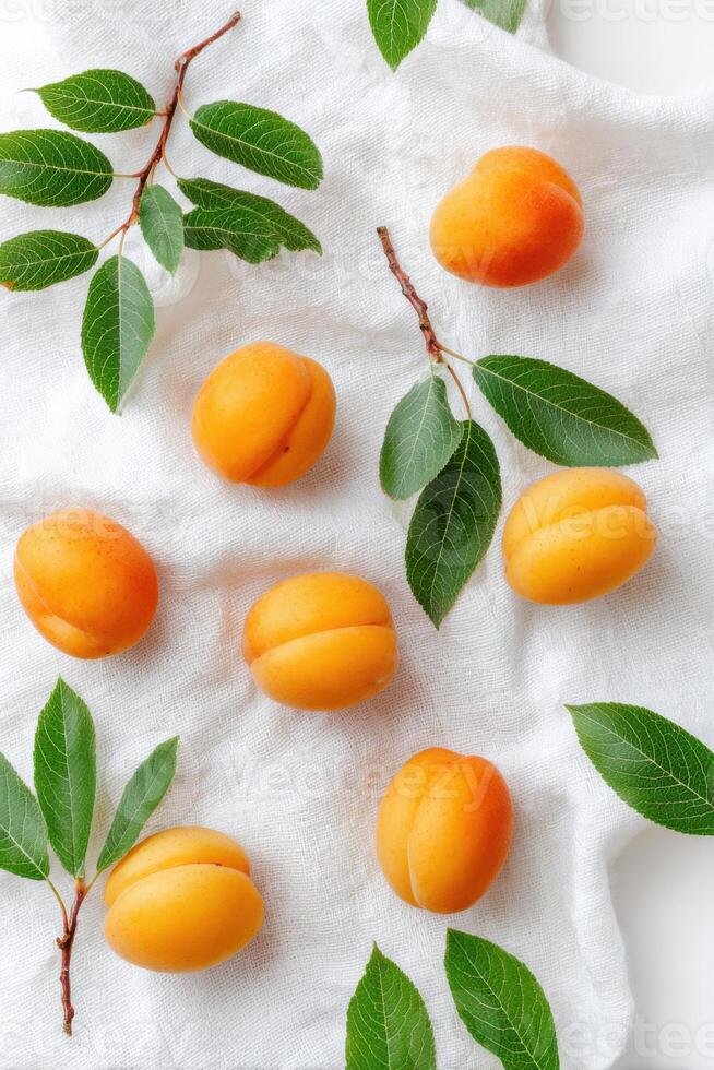 Fresh apricots arranged artistically on a textured white fabric, surrounded by vibrant green leaves, creating a visually appealing and natural composition for culinary or lifestyle themes photo
