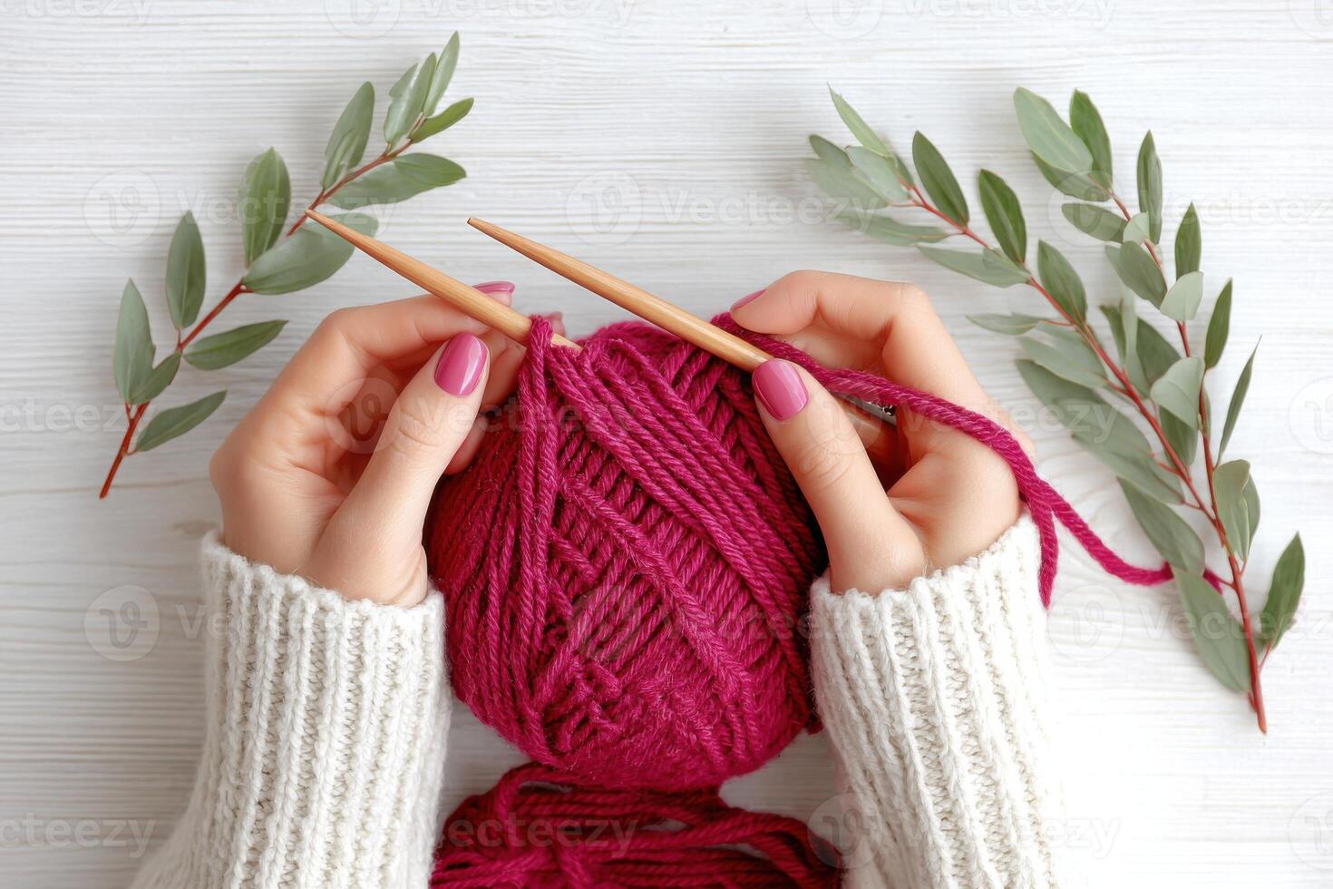 Hands of a woman holding knitting needles, working with a vibrant pink yarn ball surrounded by green leaves, showcasing a cozy crafting atmosphere and creative hobby photo