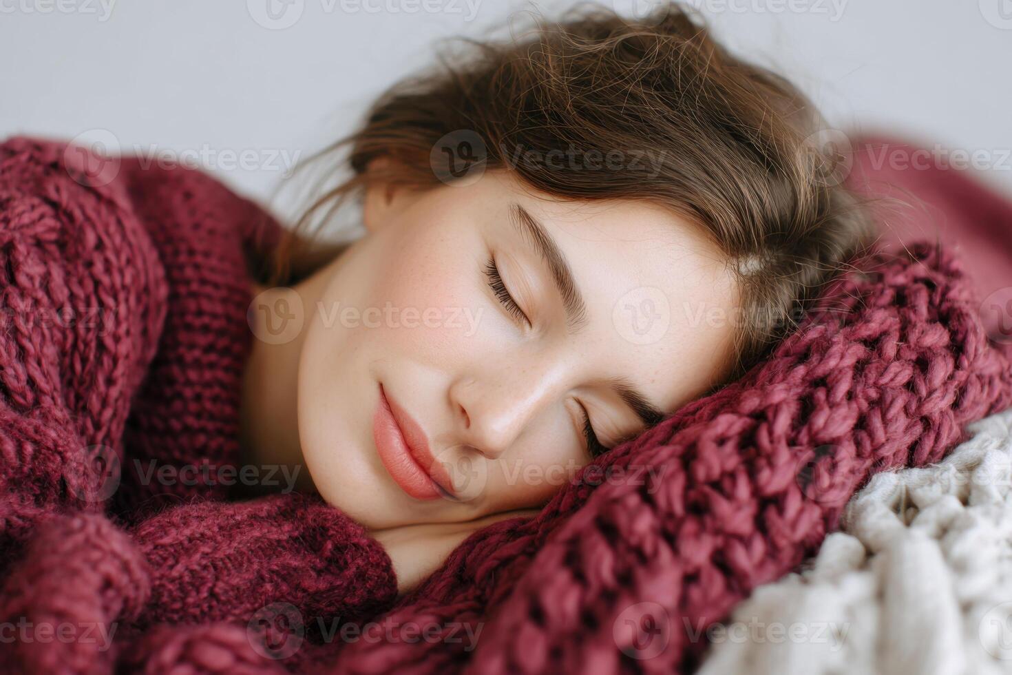 Young woman with closed eyes, resting peacefully on cozy knitted blanket, wearing warm burgundy sweater, conveying tranquility and comfort in a serene indoor atmosphere photo
