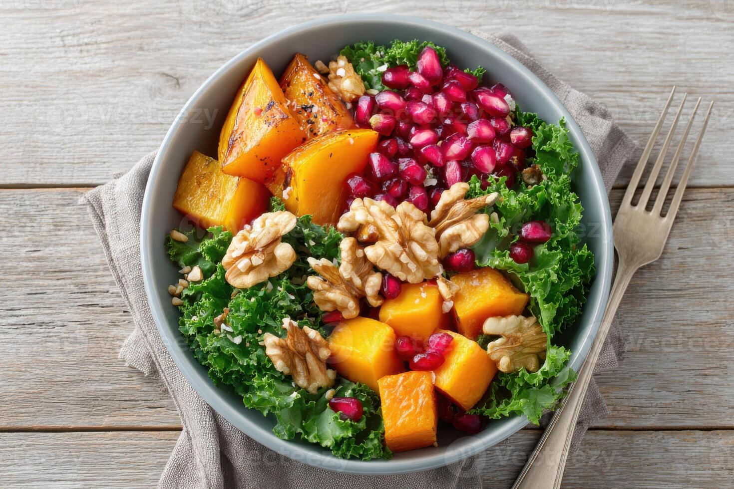 Colorful salad bowl featuring fresh kale, roasted pumpkin, pomegranate seeds, and walnuts, beautifully arranged on a rustic wooden table, showcasing healthy eating and vibrant ingredients photo
