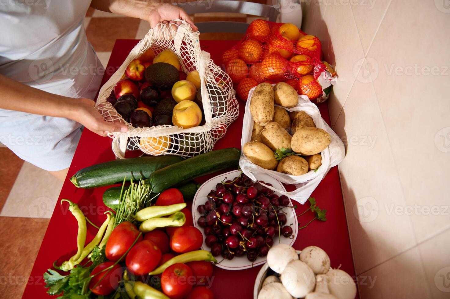 Woman Organizing Fresh Vegetables and Fruits on Kitchen Table in Eco-Friendly Bags photo