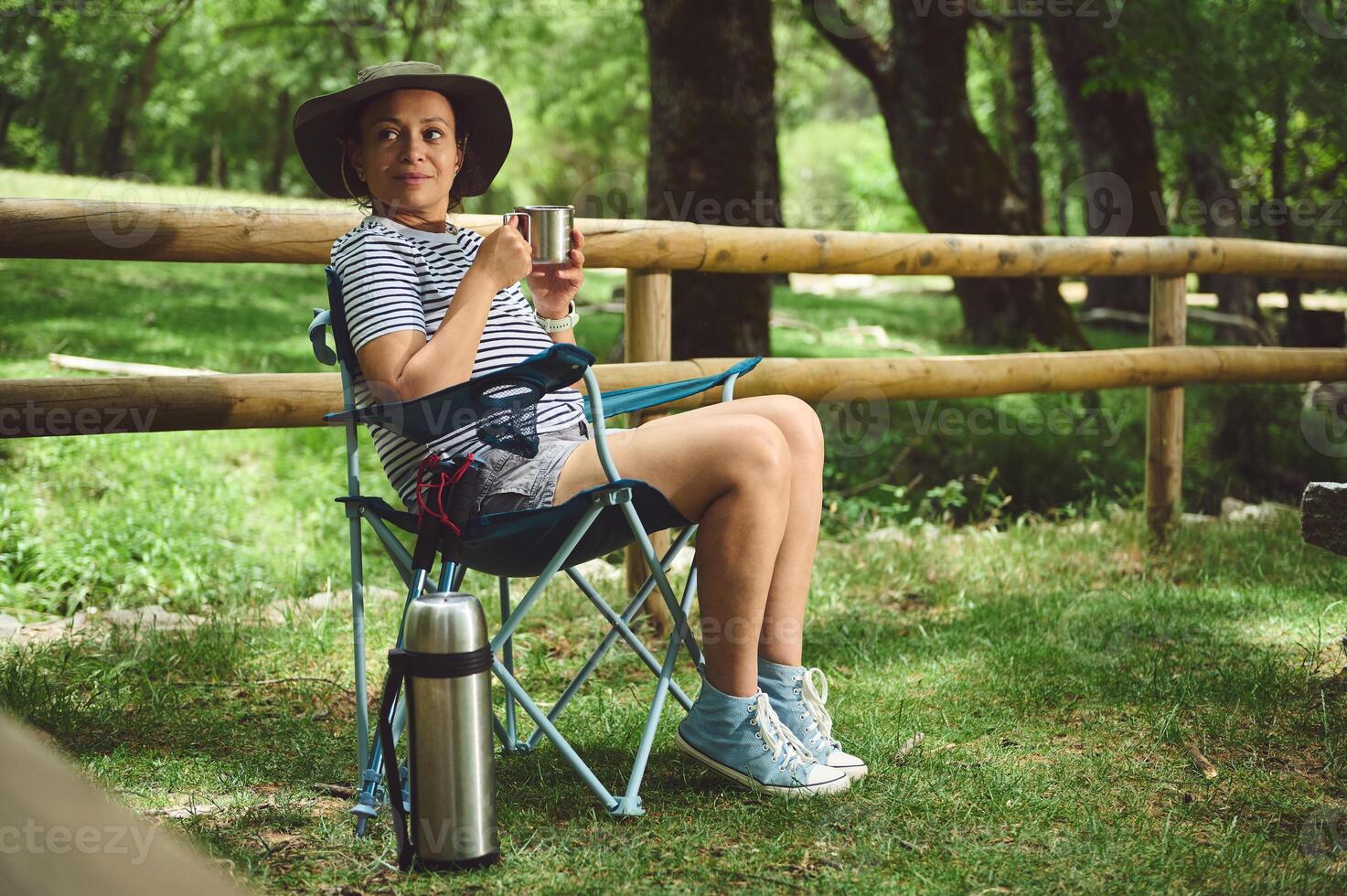 Woman Relaxing Outdoors in a Camping Chair Holding a Hot Drink in a Serene Forest Setting photo