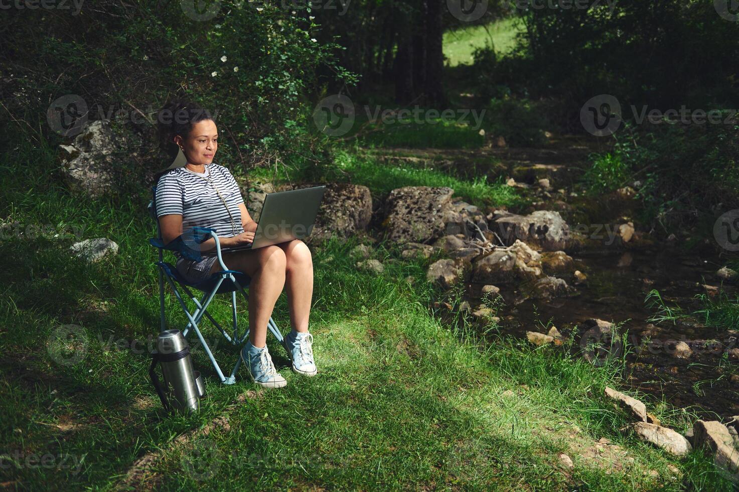Woman Working on a Laptop Outdoors by a Creek in a Scenic Forest photo