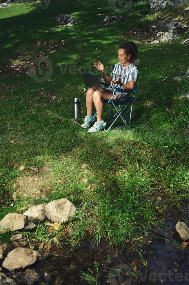 Woman Relaxing Outdoors Using a Laptop in a Natural Setting by a Calm Stream photo
