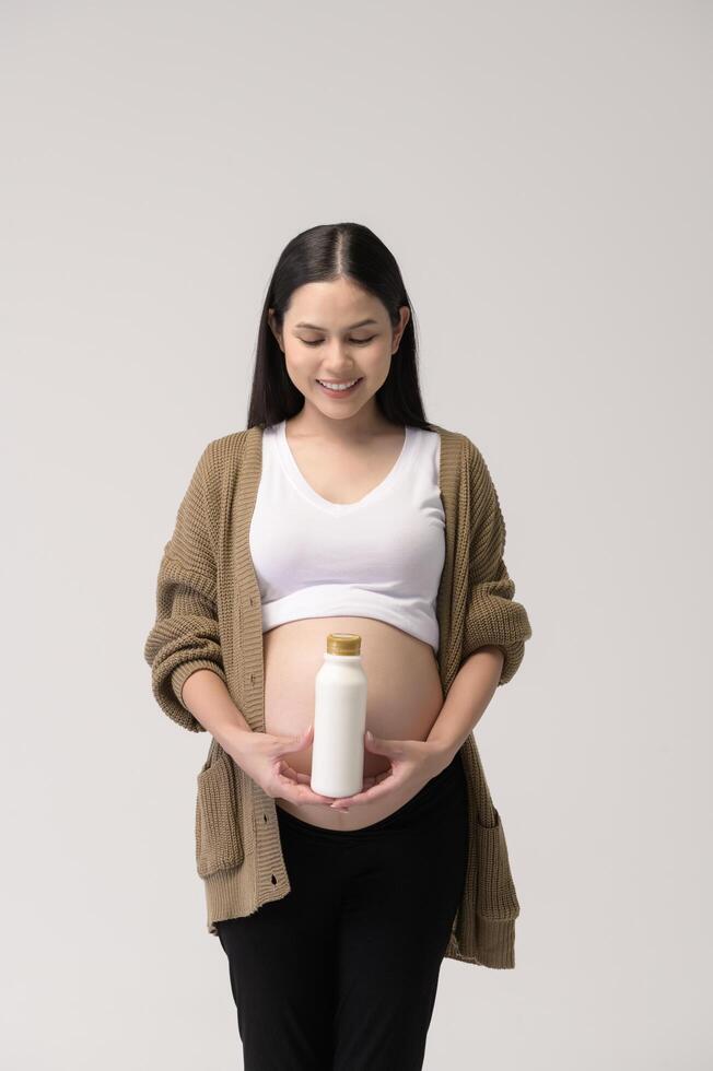 Pregnant woman drinking milk over white background studio photo