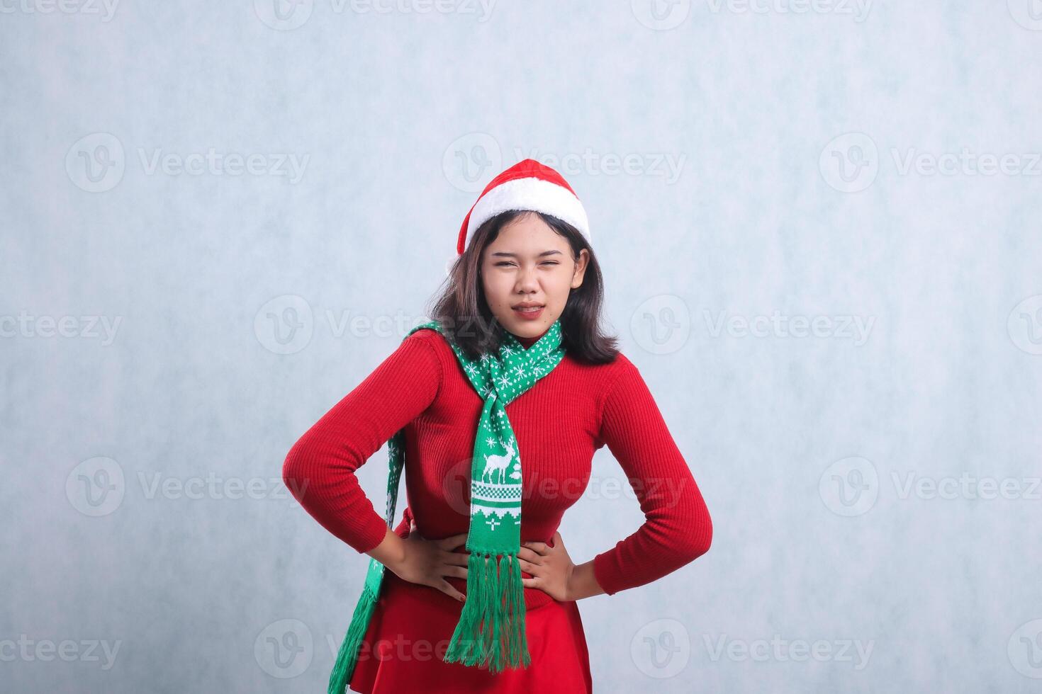 Charming young Asian ladies wearing red christmas sweater, Santa hat and scarf, looking at camera with both hands holding stomach ache, isolated on white background photo
